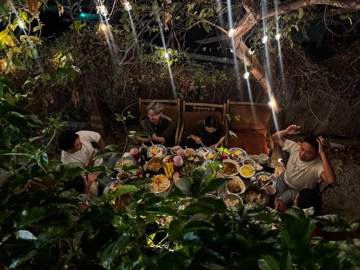 Overhead view of friends laughing around a lantern-lit dinner table surrounded by greenery